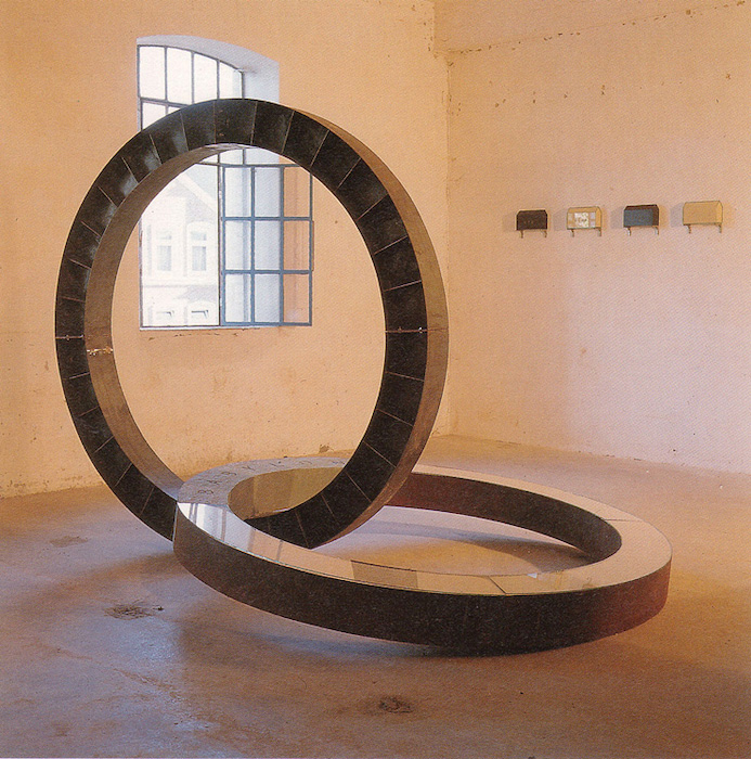 Skulptur aus einem senkrechten Stahlkreisring, darin ein liegender Kreisring mit Buchstabennudeln